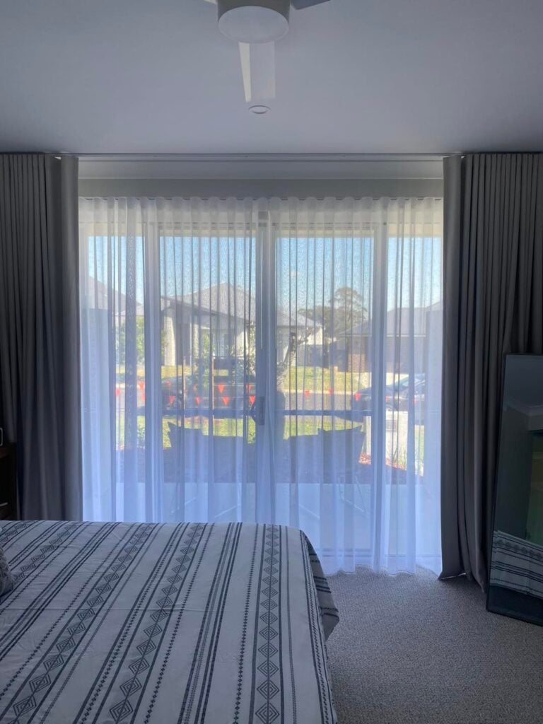 A large glass sliding door dressed with sheer white curtains in the centre and framed by solid grey blockout curtains on either side.
