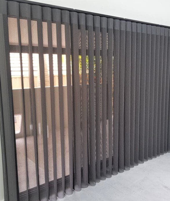A sliding glass patio door covered by dark charcoal grey vertical sheer blinds, offering a glimpse of a fenced outdoor area.