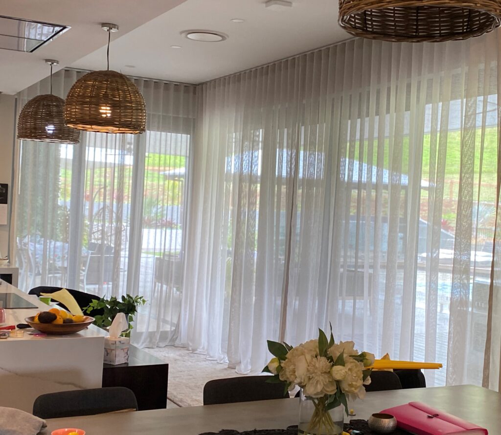 An open-plan kitchen and dining area featuring large glass doors covered by floor-to-ceiling, sheer white S-fold curtains.