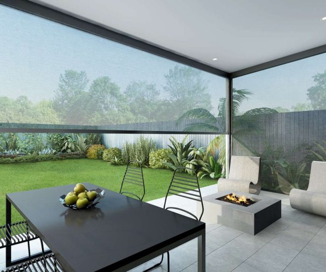 A modern covered patio featuring a dining table, a square fire pit, and lounge chairs, enclosed by large, light grey mesh privacy shades looking out onto a manicured green lawn.